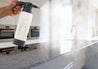 Person spraying a high-performance Kitchen and Bath Mister over a kitchen surface for cleaning.